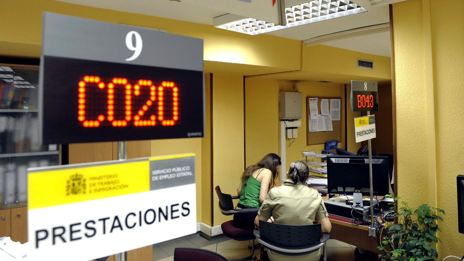 Panel digital de turnos y cartel del área de prestaciones en una oficina del Servicio Público de Empleo Estatal.