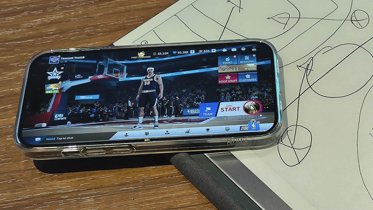 iPhone con el juego NBA Infinite en pantalla sobre cuaderno con tácticas de basket