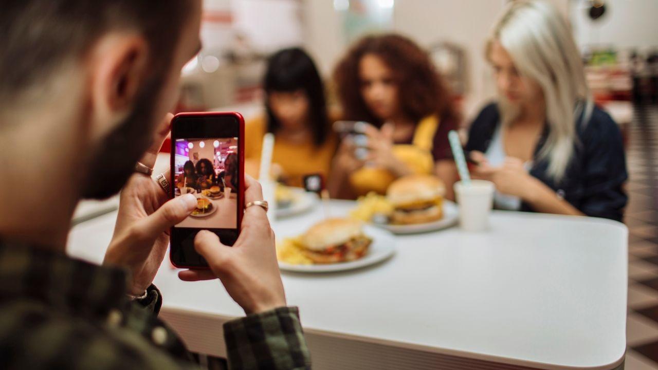 chico haciendo foto amigos comiendo en un local para instagram