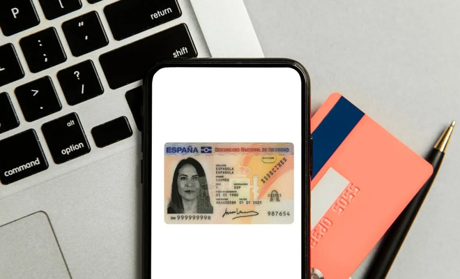 Pantalla de un teléfono móvil mostrando la imagen de un DNI electrónico español sobre un teclado de ordenador.