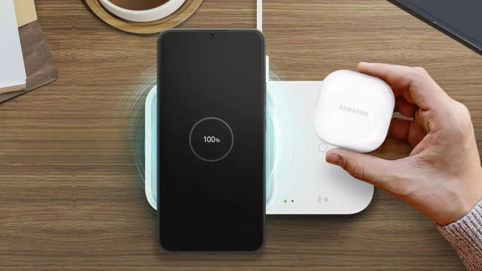 Teléfono móvil Samsung Galaxy cargando en una base inalámbrica doble junto al estuche de unos auriculares.