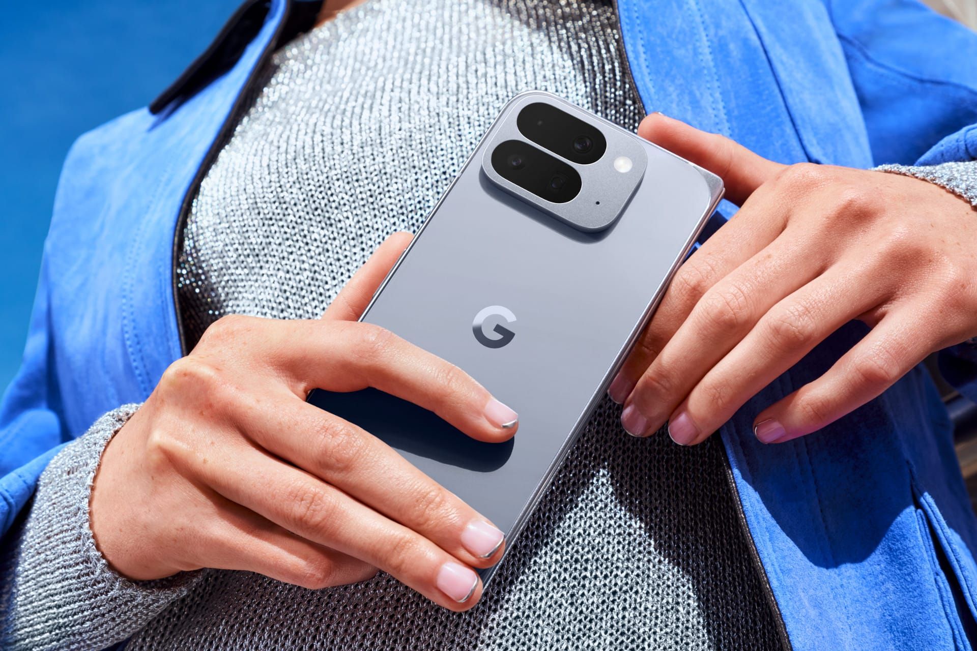 Parte trasera de un Google Pixel 10 Pro Fold en color gris sostenido con las manos sobre una prenda azul.