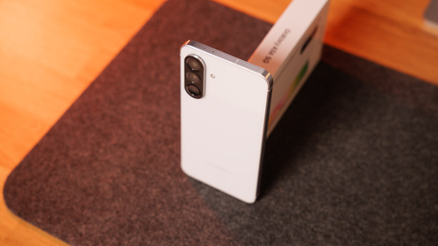 Parte trasera de un smartphone Samsung Galaxy A56 blanco con triple cámara en vertical sobre una alfombrilla oscura.