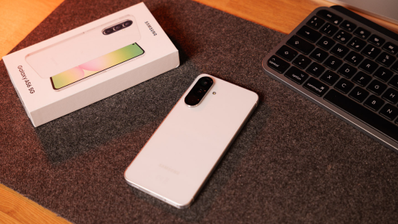 Parte trasera de un smartphone Samsung Galaxy A56 de color blanco junto a su caja oficial sobre una alfombrilla de escritorio.