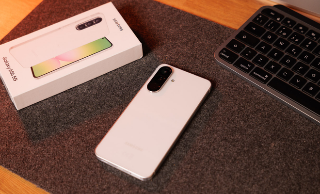 Parte trasera de un smartphone Samsung Galaxy A56 de color blanco junto a su caja oficial sobre una alfombrilla de escritorio.