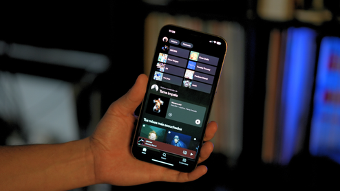 Interfaz de la aplicación Spotify abierta en un iPhone sostenido por una mano.