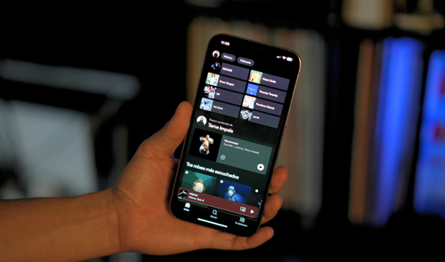 Interfaz de la aplicación Spotify abierta en un iPhone sostenido por una mano.