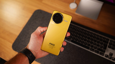 Parte trasera del smartphone POCO F7 Ultra en color amarillo sostenido con una mano sobre un escritorio.