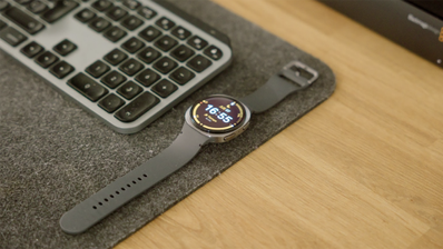 Reloj inteligente Samsung Galaxy Watch8 con esfera circular y correa oscura sobre un escritorio junto a un teclado inalámbrico.