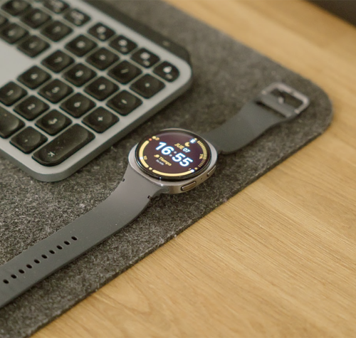 Reloj inteligente Samsung Galaxy Watch8 con esfera circular y correa oscura sobre un escritorio junto a un teclado inalámbrico.