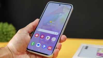 Mano sujetando un Samsung Galaxy A35 encendido mostrando la pantalla de inicio con iconos de aplicaciones y widget de clima.