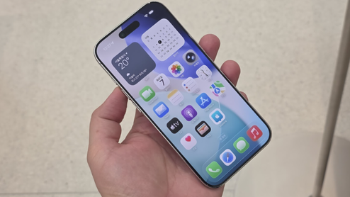 iPhone 17 sostenido con una mano mostrando la pantalla de inicio con widgets de tiempo y calendario.
