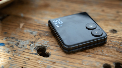 Teléfono plegable Xiaomi Mix Flip cerrado sobre una mesa de madera mostrando su pantalla externa con reloj y cámaras.