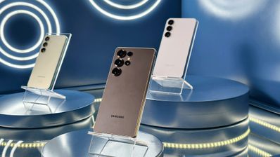 Tres smartphones Samsung Galaxy S25 dispuestos en soportes sobre peanas circulares en un entorno de exposición con iluminación azul.