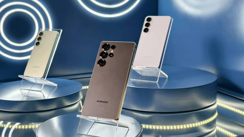 Tres smartphones Samsung Galaxy S25 dispuestos en soportes sobre peanas circulares en un entorno de exposición con iluminación azul.