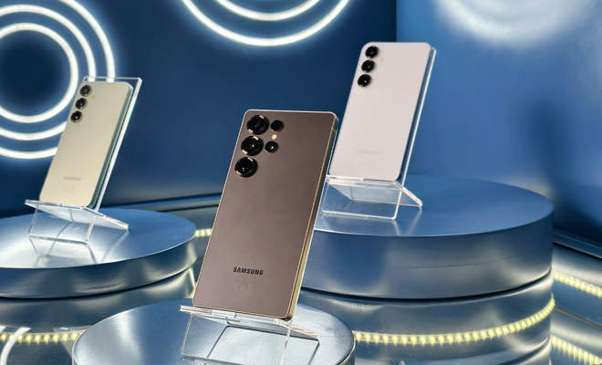 Tres smartphones Samsung Galaxy S25 dispuestos en soportes sobre peanas circulares en un entorno de exposición con iluminación azul.