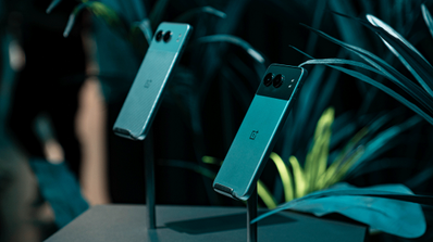 Parte trasera de dos smartphones OnePlus Nord 4 en soportes de exposición sobre un fondo de vegetación.