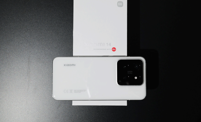 Parte trasera de un Xiaomi 14 de color blanco con su módulo de cámaras cuadrado sobre su caja de venta original sobre un fondo oscuro.