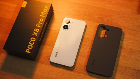 Parte trasera del teléfono POCO X8 Pro Max en color blanco junto a su caja y una funda protectora negra sobre una mesa de madera.