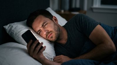 Hombre en la cama dolorido mirando el móvil.