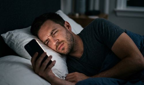Hombre en la cama dolorido mirando el móvil.