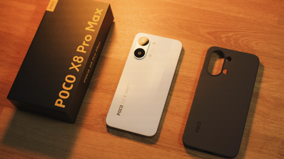 Parte trasera del teléfono POCO X8 Pro Max en color blanco junto a su caja y una funda protectora negra sobre una mesa de madera.