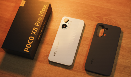 Parte trasera del teléfono POCO X8 Pro Max en color blanco junto a su caja y una funda protectora negra sobre una mesa de madera.