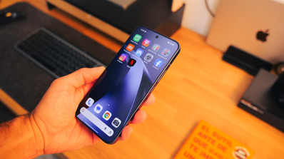 Mano sujetando un smartphone Xiaomi con la pantalla encendida mostrando iconos de aplicaciones sobre un escritorio de madera.