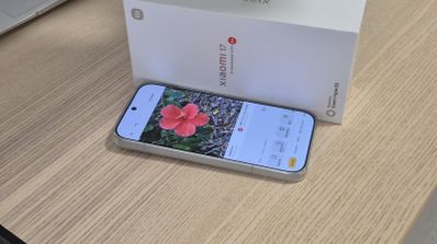 Teléfono Xiaomi 17 mostrando una fotografía de una flor roja en su pantalla junto a su caja blanca de venta al público.