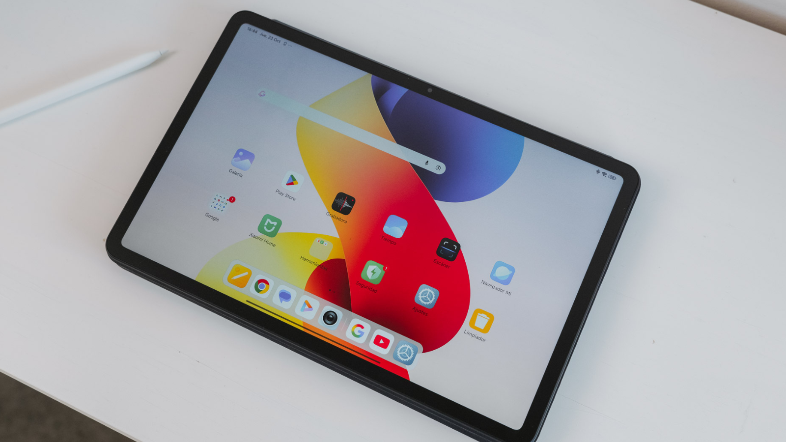 Tableta Redmi Pad 2 Pro encendida sobre una mesa blanca mostrando la interfaz de usuario con iconos de aplicaciones y un lápiz óptico al lado.