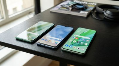 Tres teléfonos inteligentes OnePlus dispuestos en una mesa mostrando diferentes interfaces de usuario.