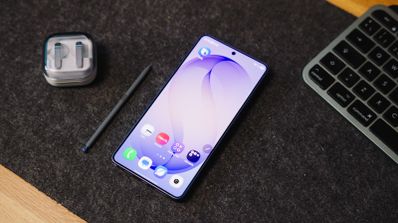 Frontal del Samsung Galaxy S26 Ultra encendido sobre un escritorio junto a su puntero óptico y unos auriculares.