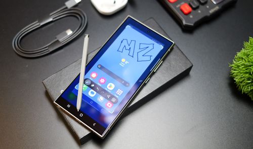 Smartphone Samsung Galaxy S24 Ultra con pantalla encendida apoyado sobre su caja junto al lápiz óptico S Pen y un cable USB-C.