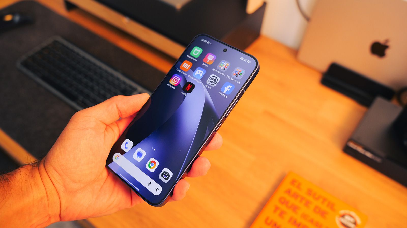 Mano sujetando un teléfono Xiaomi 17T Pro encendido mostrando la pantalla de inicio con iconos de aplicaciones sobre un escritorio de madera.