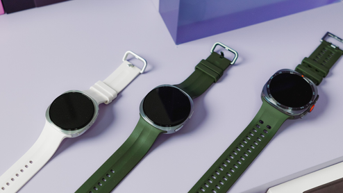 Tres relojes inteligentes Samsung Galaxy Watch alineados en diagonal sobre una superficie violeta, mostrando correas en color blanco y verde oliva.