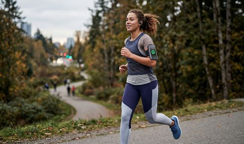 Mujer corriendo por un sendero con un brazalete para móvil que muestra la aplicación de Spotify.