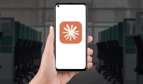Mano sosteniendo un teléfono móvil que muestra el logotipo de la aplicación Claude sobre un fondo de oficina.