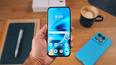 Vista frontal del Motorola Moto G87 sostenido con una mano sobre una mesa de madera con accesorios.