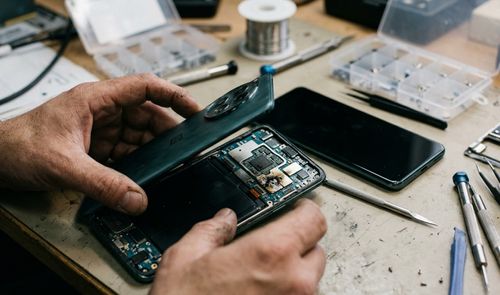 Primer plano de un técnico manipulando un smartphone OnePlus 12 abierto con daños por quemaduras en los circuitos internos.