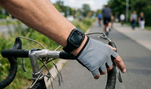Primer plano de un ciclista con guantes grises y el reloj inteligente TRAUSI en la muñeca mientras sujeta el manillar de una bicicleta.
