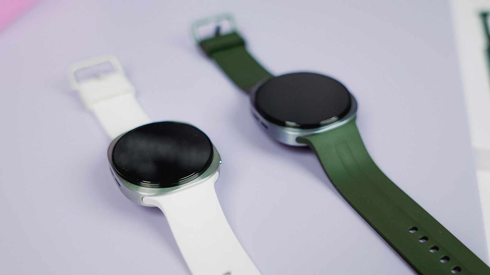 Dos relojes inteligentes Samsung Galaxy Watch 9 con esferas circulares y correas de color blanco y verde oscuro sobre una superficie clara.
