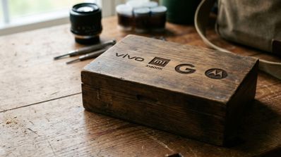 Caja de madera con logotipos de Vivo, Xiaomi, Google y Motorola grabados en la tapa sobre una mesa de trabajo.