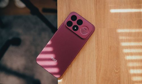 Parte trasera de un teléfono POCO F9 Ultra en color rojo cherry apoyado sobre una mesa de madera con sombras de persiana.