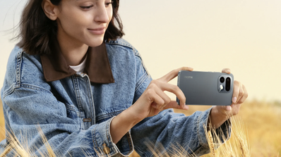 Mujer joven con chaqueta vaquera sosteniendo el smartphone realme 16 Pro en posición horizontal en un campo de trigo.