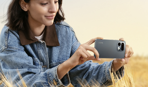 Mujer joven con chaqueta vaquera sosteniendo el smartphone realme 16 Pro en posición horizontal en un campo de trigo.