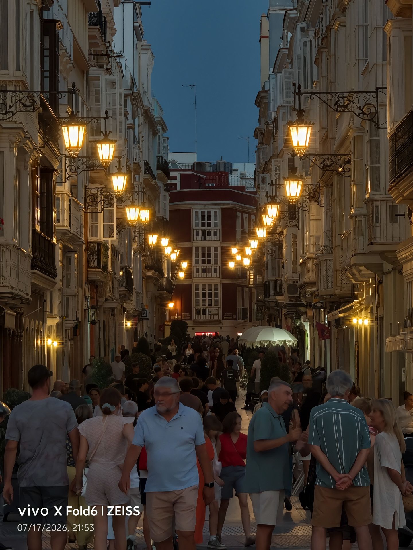 Calle peatonal concurrida al anochecer con farolas encendidas y edificios clásicos, fotografiada con un vivo X Fold6.