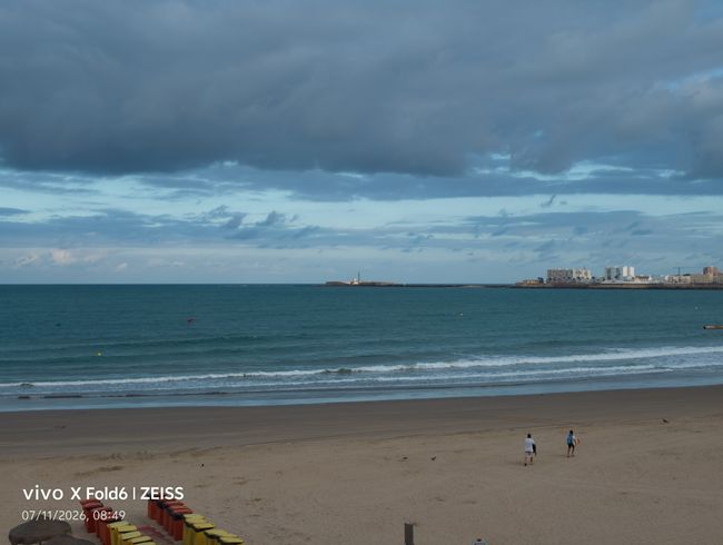Playa de arena bajo un cielo con densas nubes grises y el mar en calma, capturada con un vivo X Fold6.