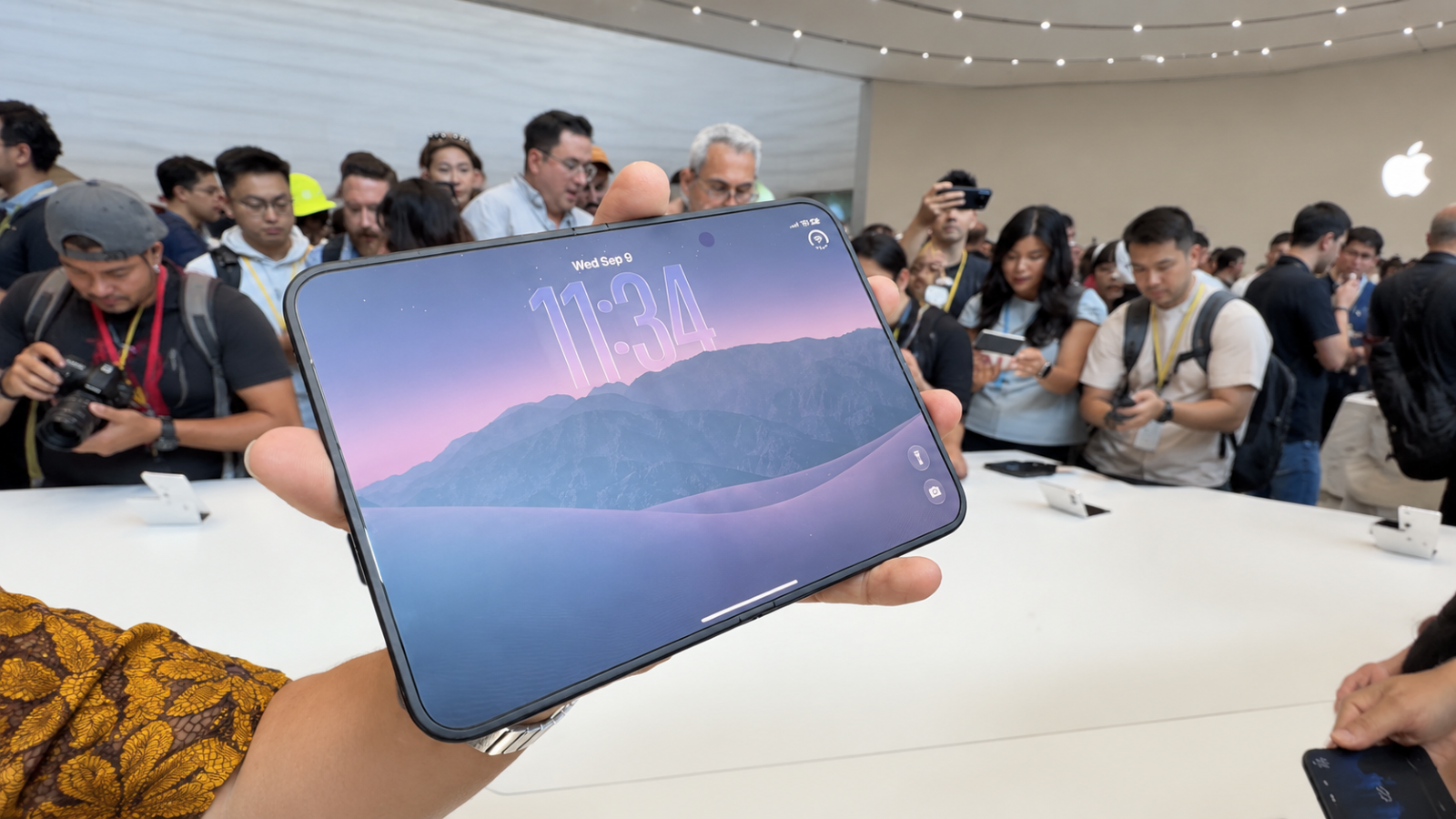 Primer plano de la pantalla desplegada del iPhone Duo en un evento de presentación con público al fondo.