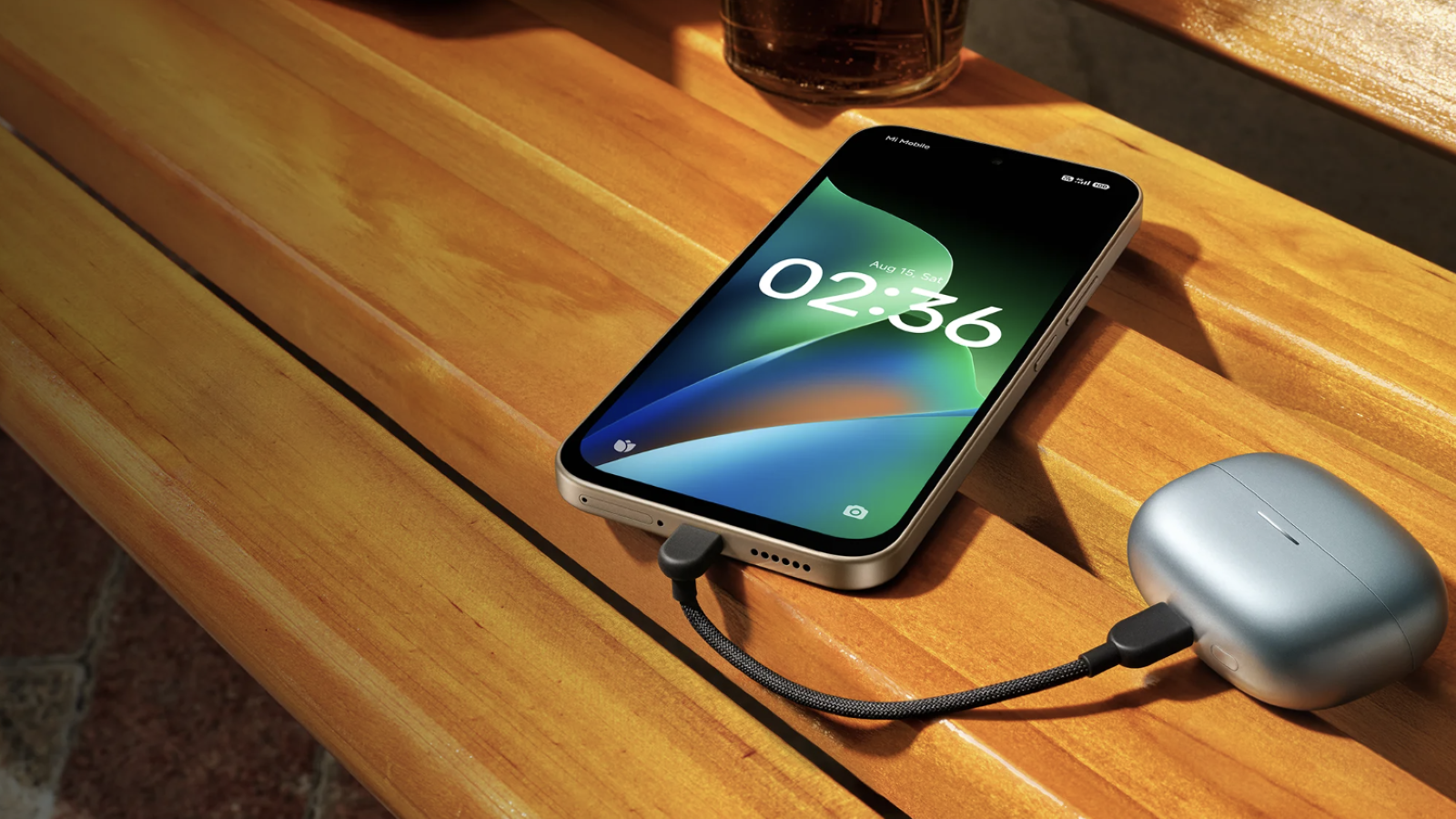 Teléfono Redmi 17 4G conectado mediante un cable USB-C a un estuche de auriculares inalámbricos sobre una mesa de madera.