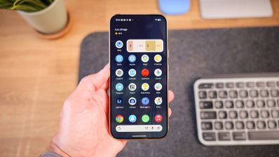 Mano sujetando un Google Pixel 11 Pro mostrando el menú de aplicaciones de Android 17 sobre un escritorio.